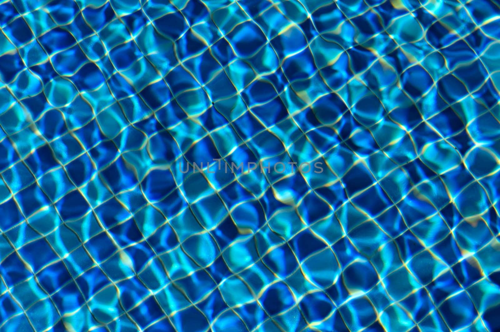 Gentle waves ripple across the deep blue surface of a pool, reflecting sunlight and creating mesmerizing patterns.