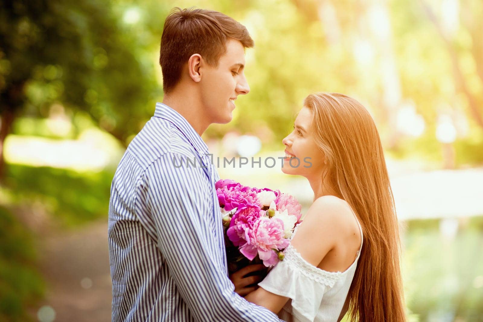 Celebrating anniversary together. Loving couple with bouquet of peony flowers at park on summer day
