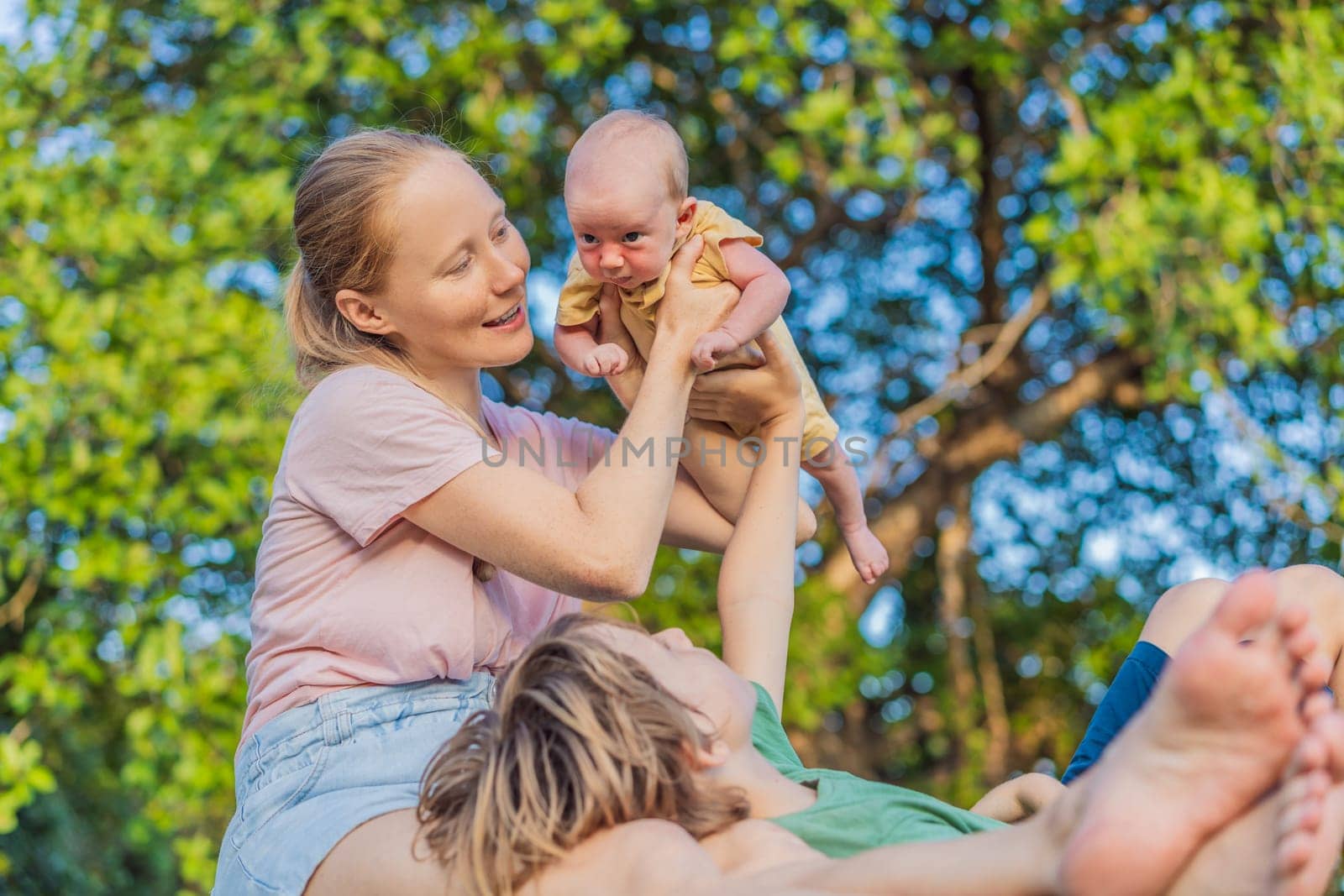 Young mother, teenage son, and one-month-old baby enjoying quality family time in the park. Multigenerational bonding and outdoor family love concept.