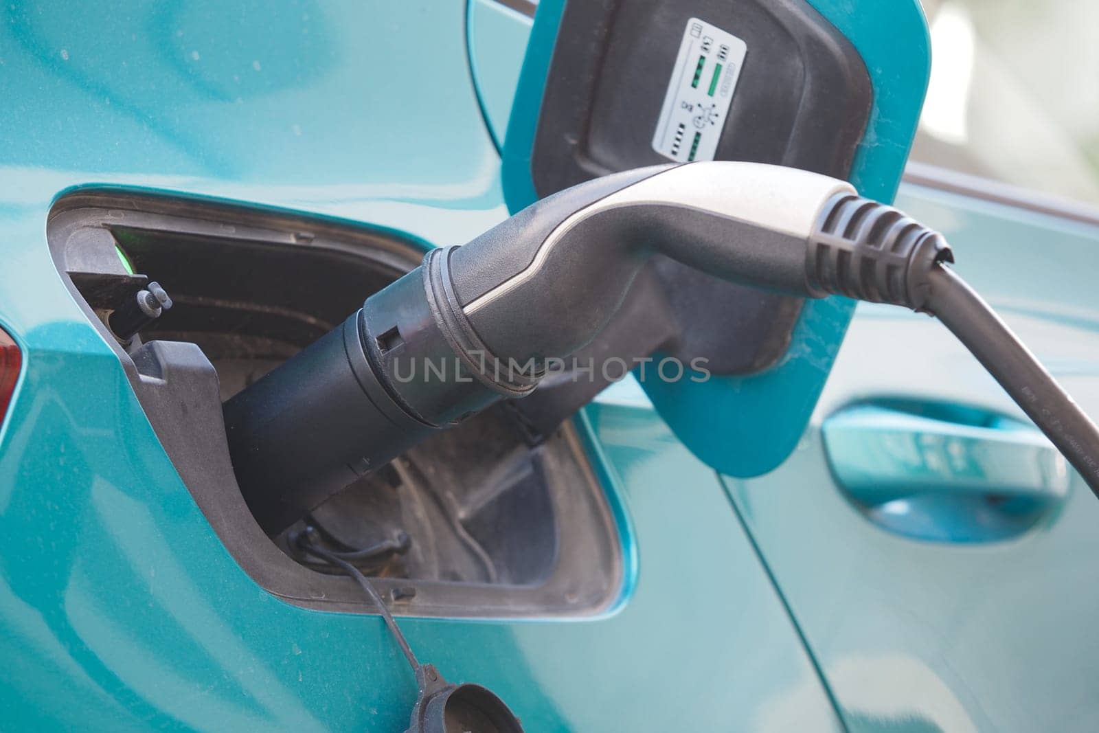 A modern electric vehicle connects to a charging station in bright daylight.