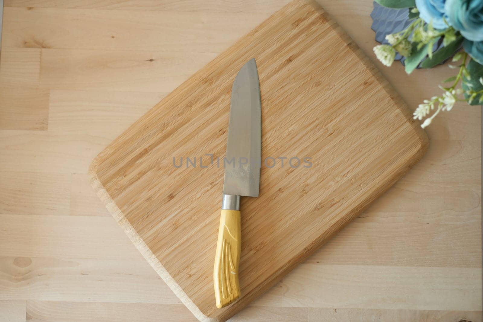 A sharp kitchen knife rests on a bamboo cutting board surrounded by decor.