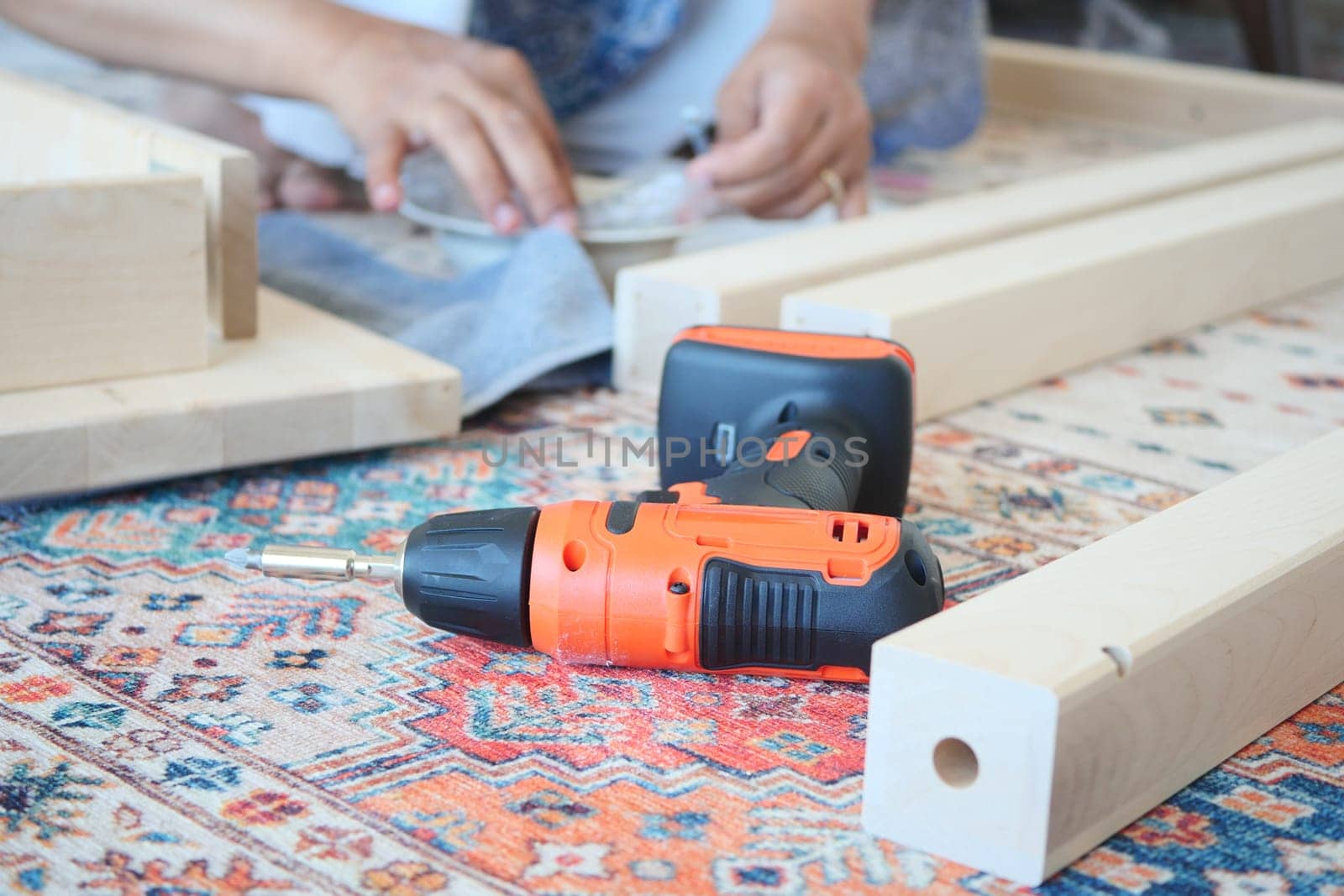 A person assembles wooden pieces using a power drill and tools.