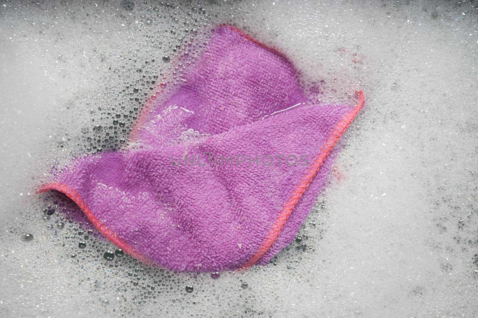 A purple cleaning cloth soaked in soapy water, ready for dishwashing.