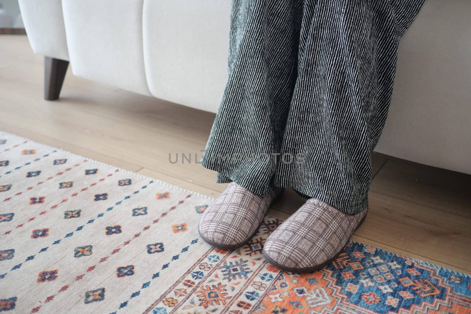 A person relaxes on a couch with feet on a colorful rug.