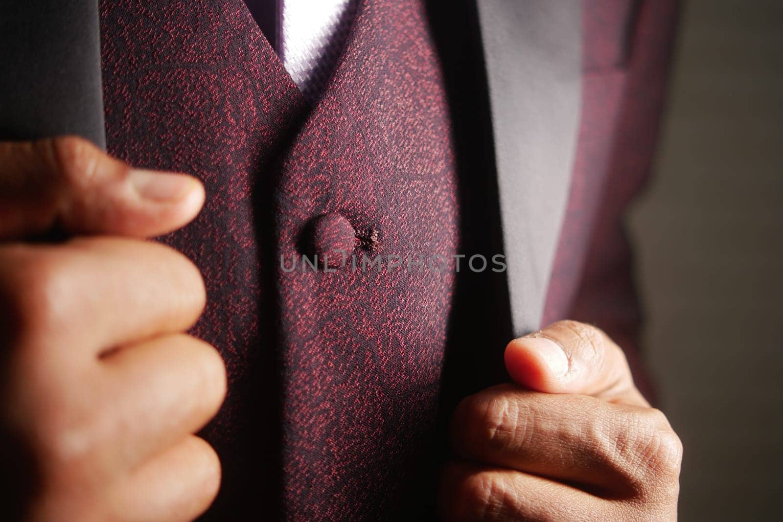 A well-dressed person adjusts their burgundy jacket, radiating style.