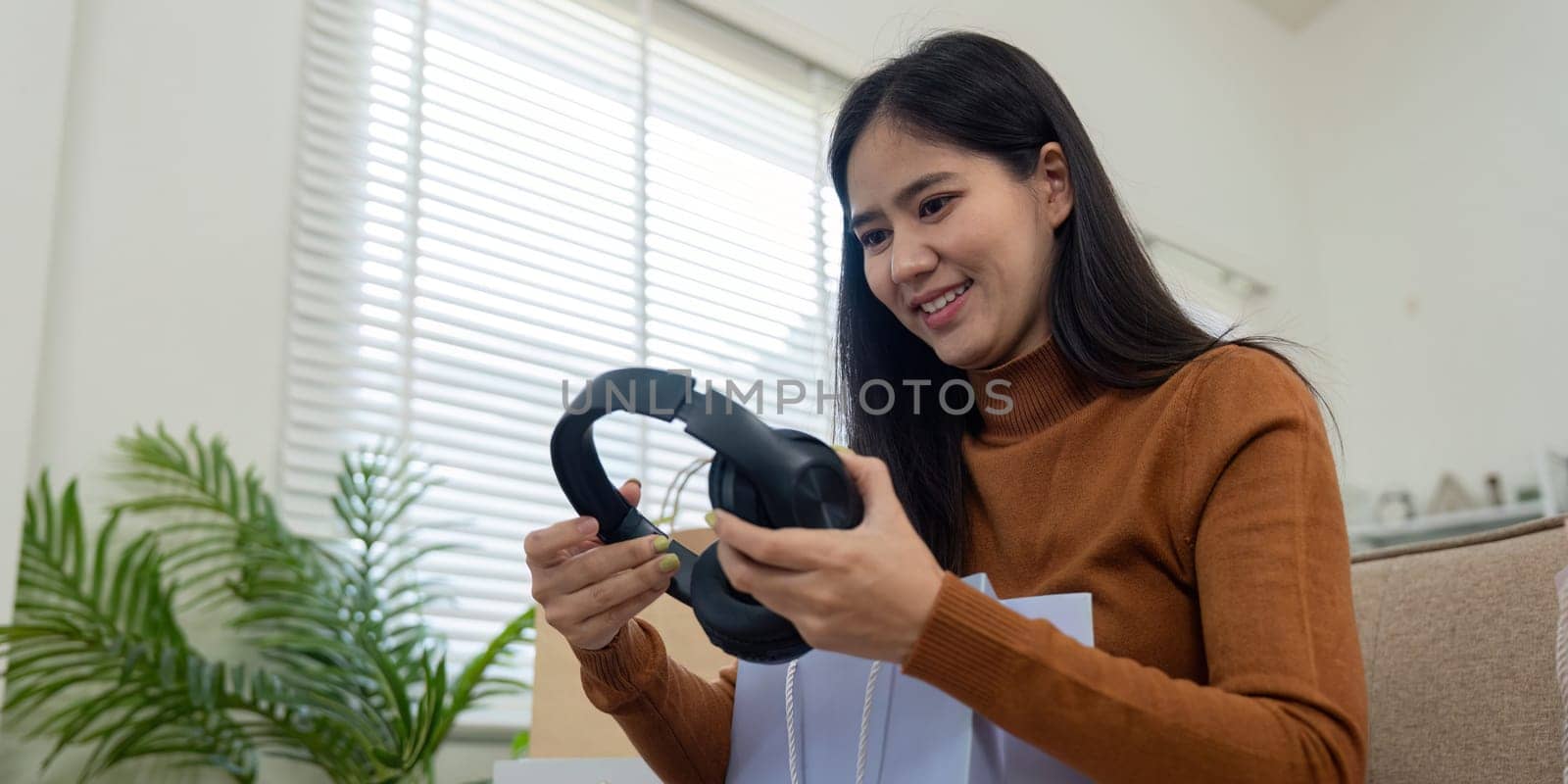 A happy woman enjoys her shopping haul, unboxing new headphones from a bag at home. Surrounded by shopping bags, she expresses delight in her finds.