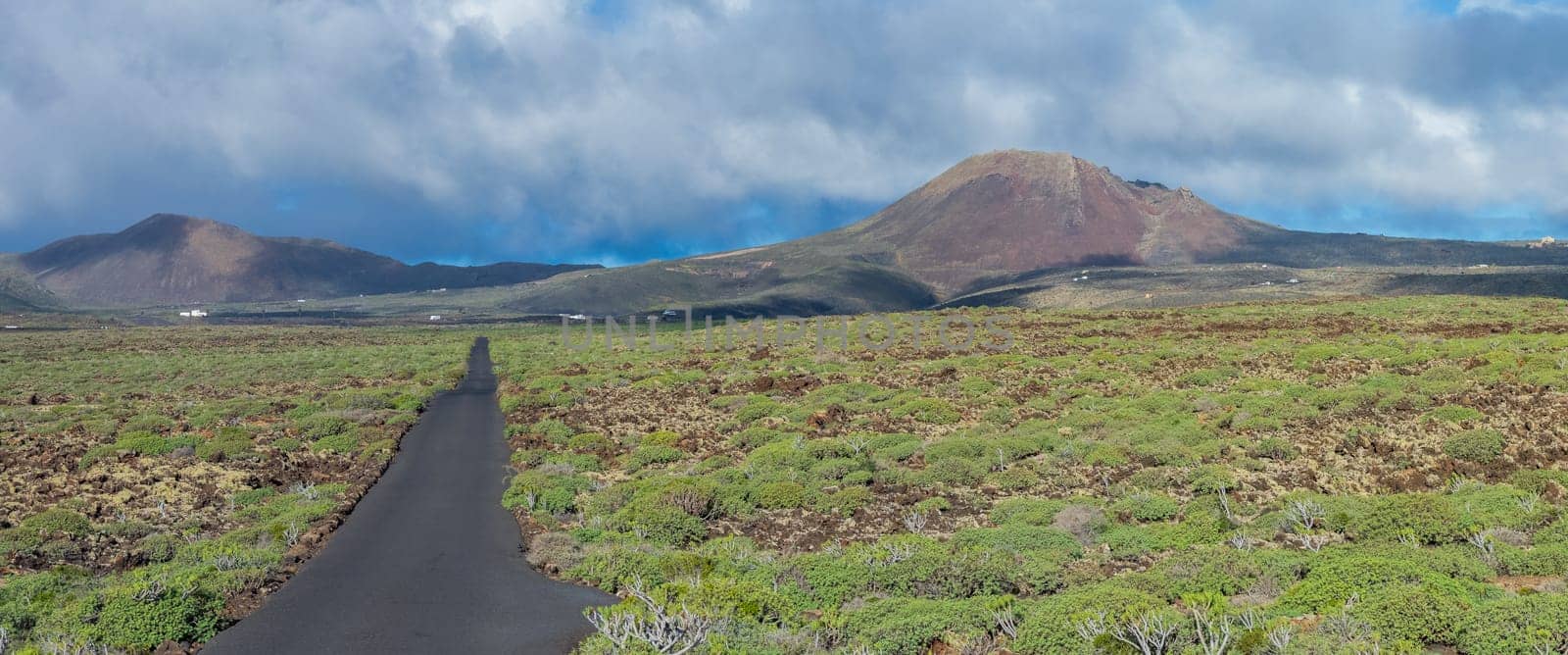 A winding road through lush greenery leads to a distant volcano under a dramatic sky, embodying isolation and adventure.
