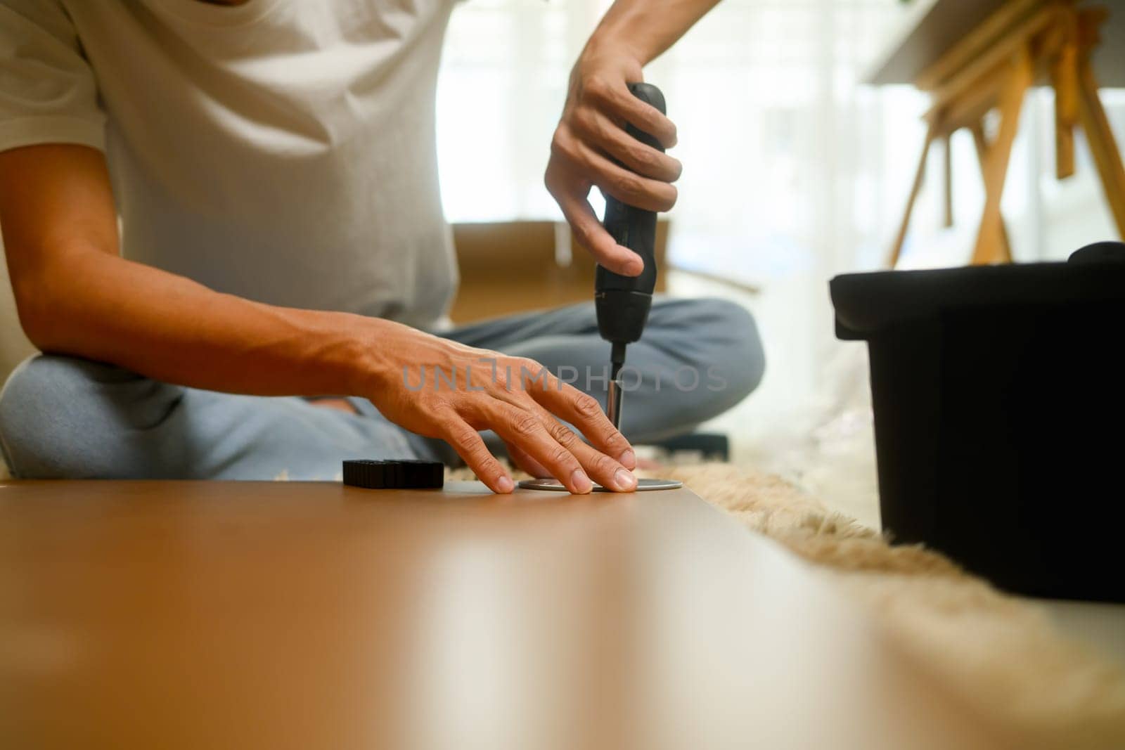 Focused Young homeowner assembling a new table, using a drill and tools to secure the legs.