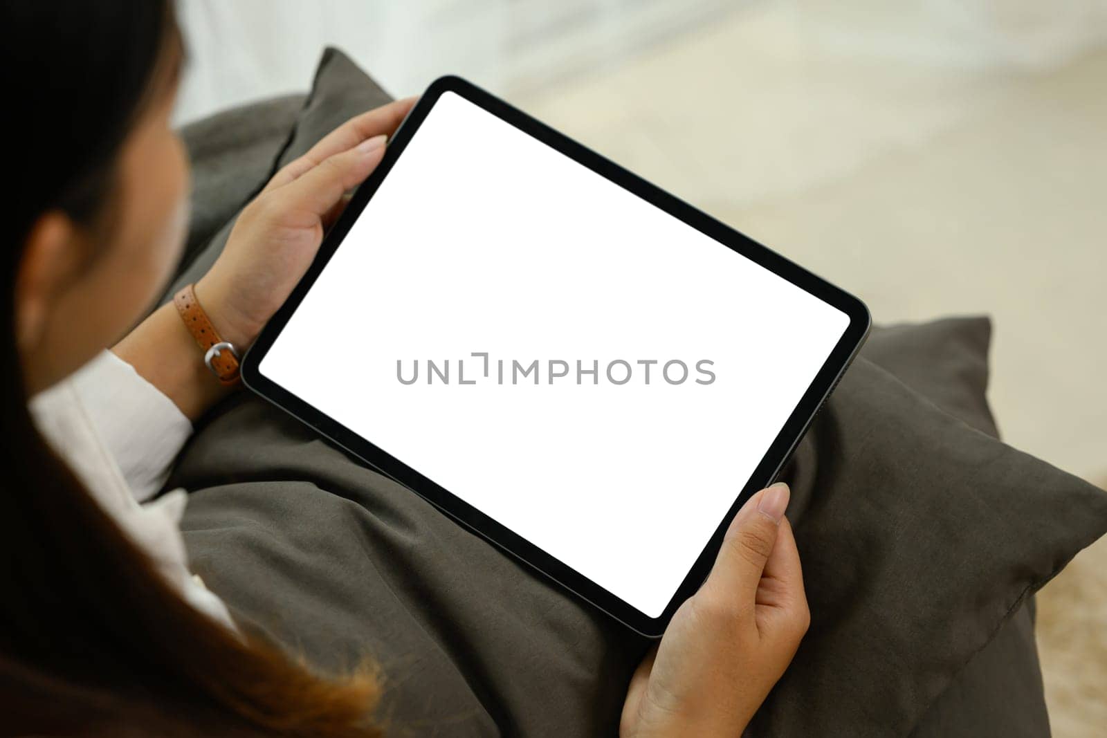 Close up of woman holding digital tablet with an empty screen sitting on a couch.