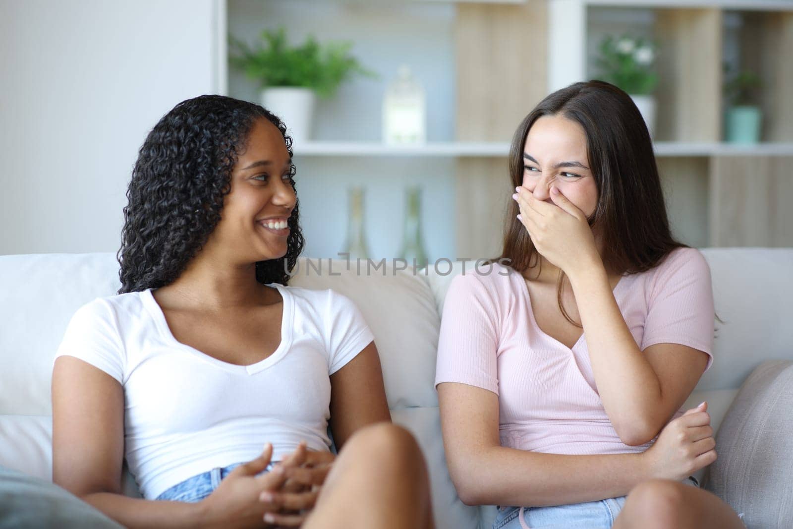 Embarrassed woman laughing covering mouth with hand talking with a friend at home