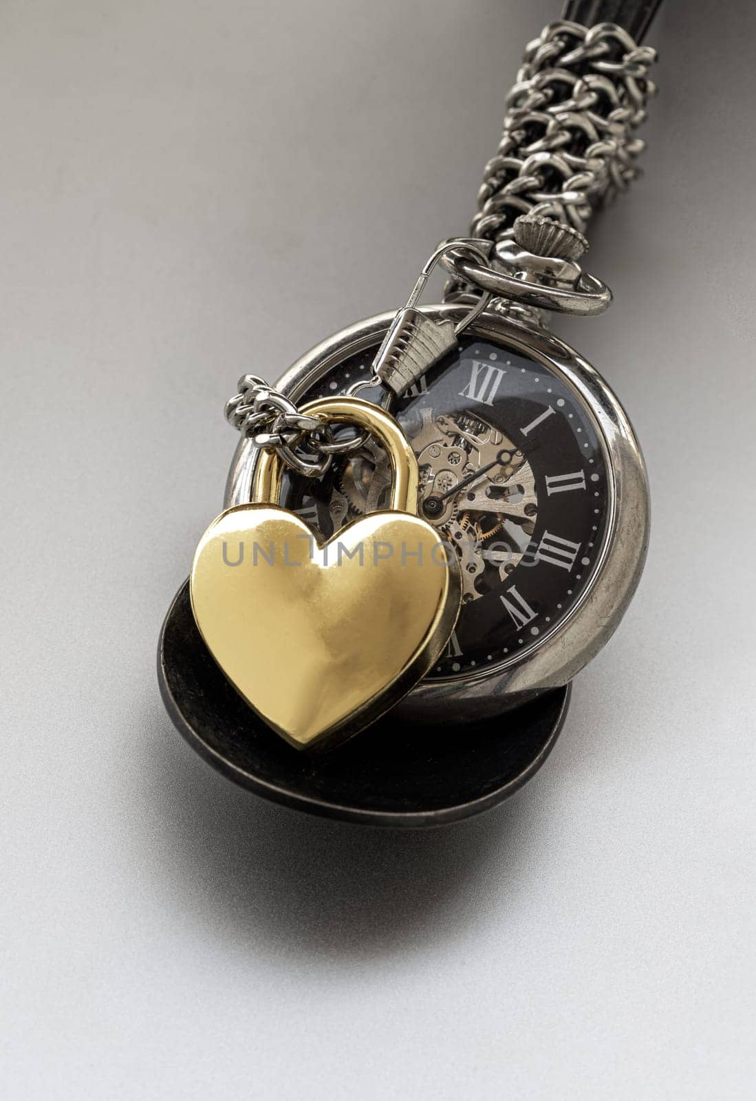 Bangkok, Thailand - Feb 09, 2025 - Golden heart shaped love padlock lap over A retro pocket watch on white background. Love can endure beyond the limitations of time, Concept of Love that transcends time, Valentine's day, use it as your Copy space, Design, Wallpaper and Poster, Selective focus.