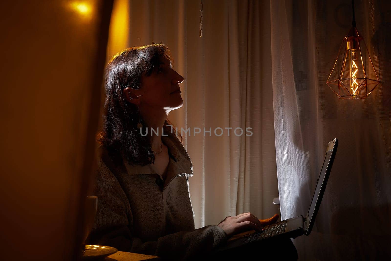A middle-aged woman relaxes in her warm, inviting home as she engages with her laptop, appreciating the peaceful evening atmosphere.