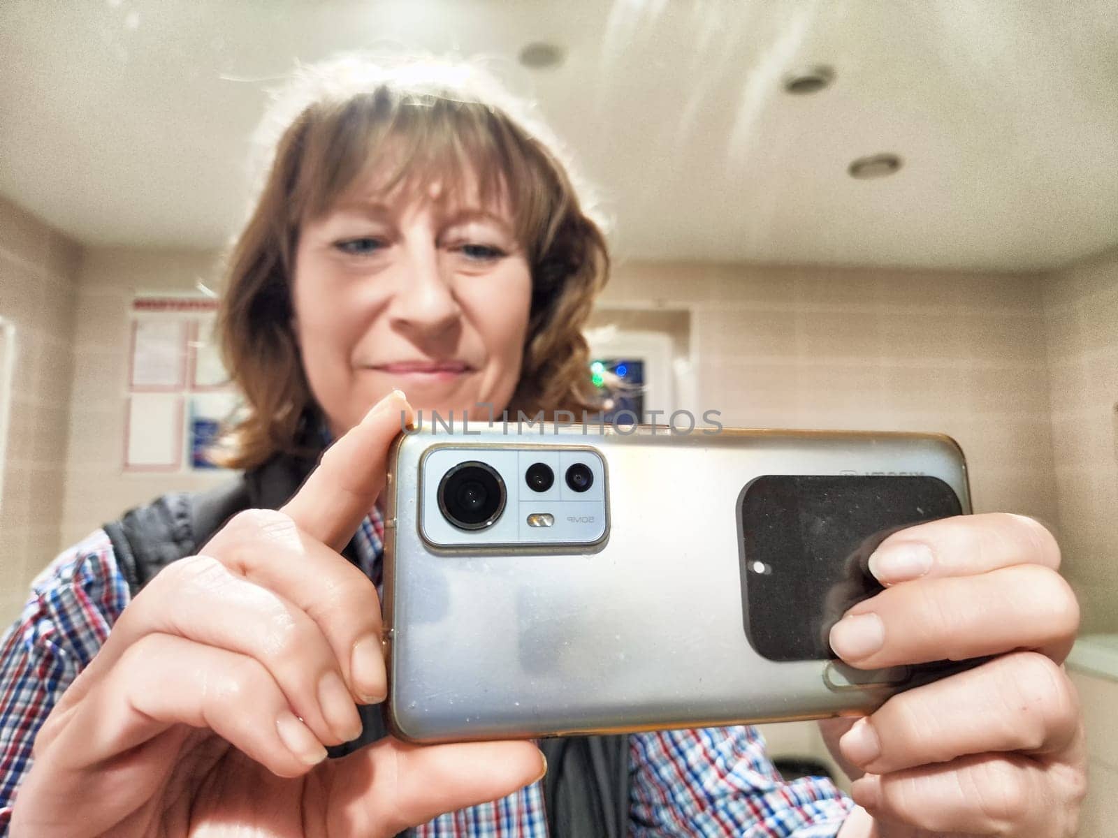 A middle-aged woman takes a cheerful selfie in the mirror, enjoying a moment of reflection in the morning light.