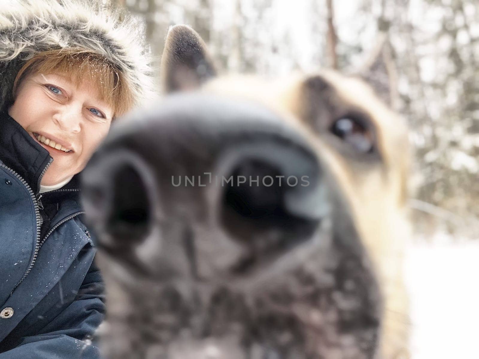 A woman enjoys a winter day with her dog, capturing the joyful atmosphere in a snow-covered forest.