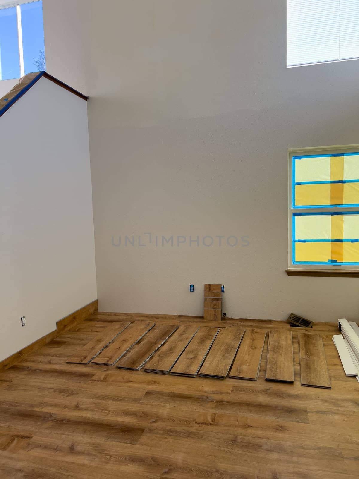 Broomfield, Colorado, USA-February 22, 2025-A living room undergoing flooring installation with partially laid wood laminate planks. The room has high ceilings, large windows covered with protective film, and construction materials neatly arranged. The image captures the progress of a home renovation project focused on updating the flooring.