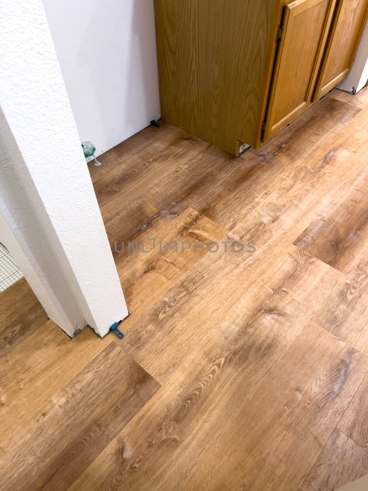 Broomfield, Colorado, USA-February 23, 2025-A kitchen undergoing flooring installation, featuring newly laid wood planks extending through the space. The underlayment is partially visible, with red tape securing it. Wooden cabinets line the kitchen, and installation tools are placed on the floor, indicating an ongoing renovation project.