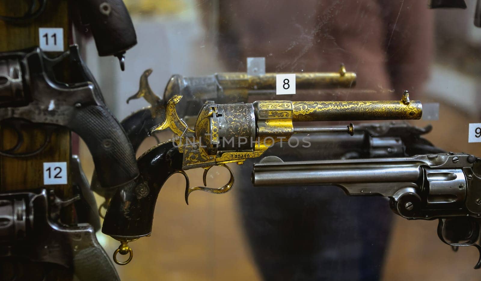 An array of antique revolvers, showcasing detailed craftsmanship, is exhibited behind glass in a vintage firearms shop.