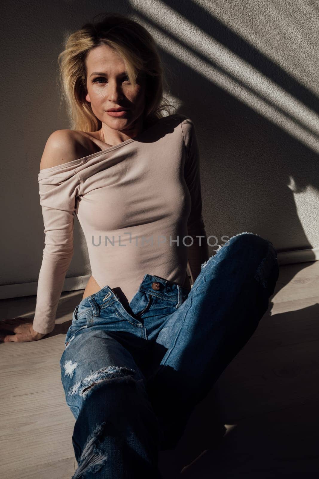 Beautiful slim fashion blonde woman in jeans by the window