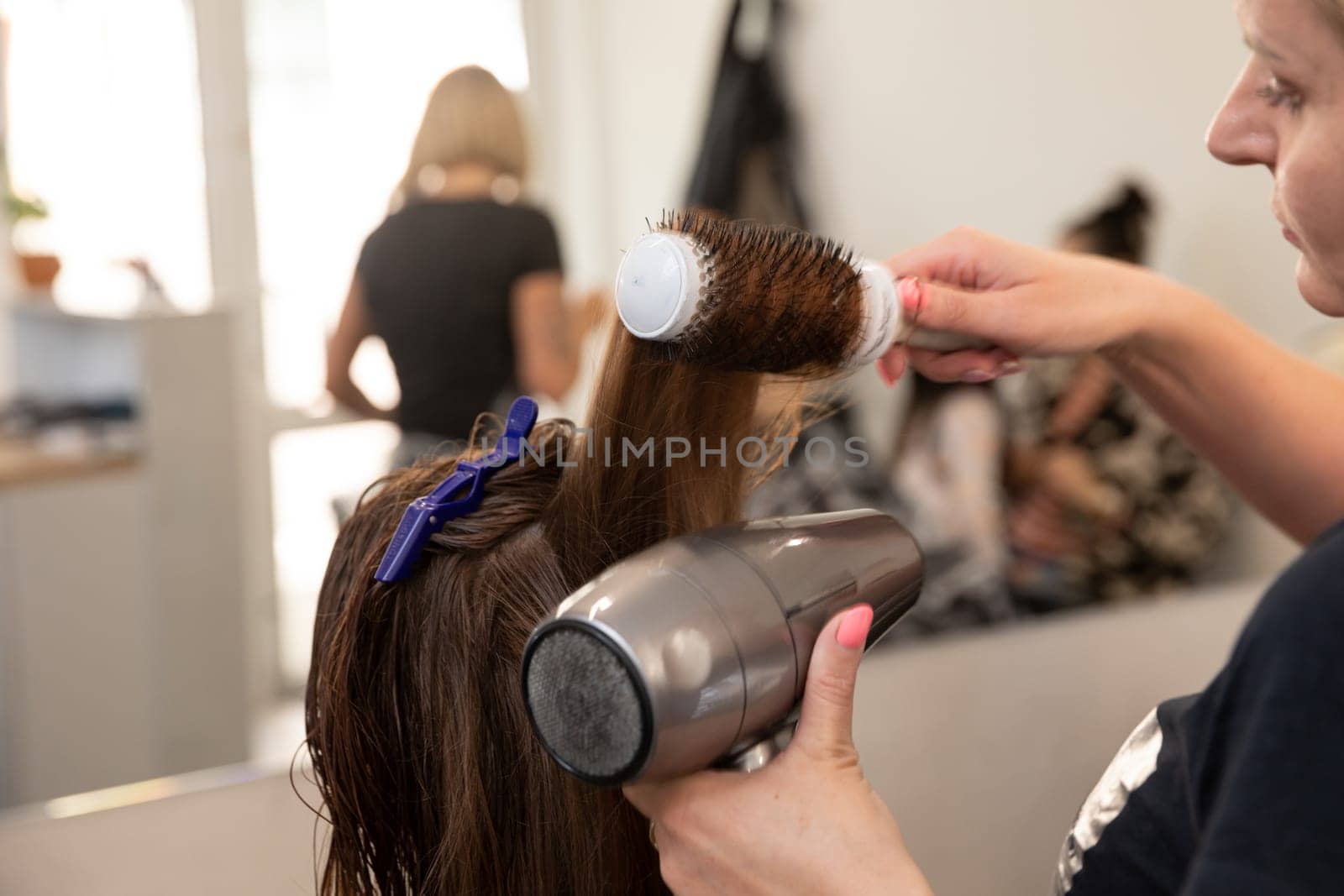 A skilled hairdresser is expertly styling a clients hair using a blow dryer and a round brush in a chic modern salon