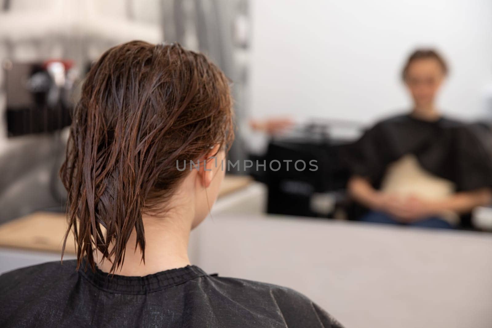 A person in a salon is waiting for their haircut, with wet hair and showcasing a vibrant beauty routine