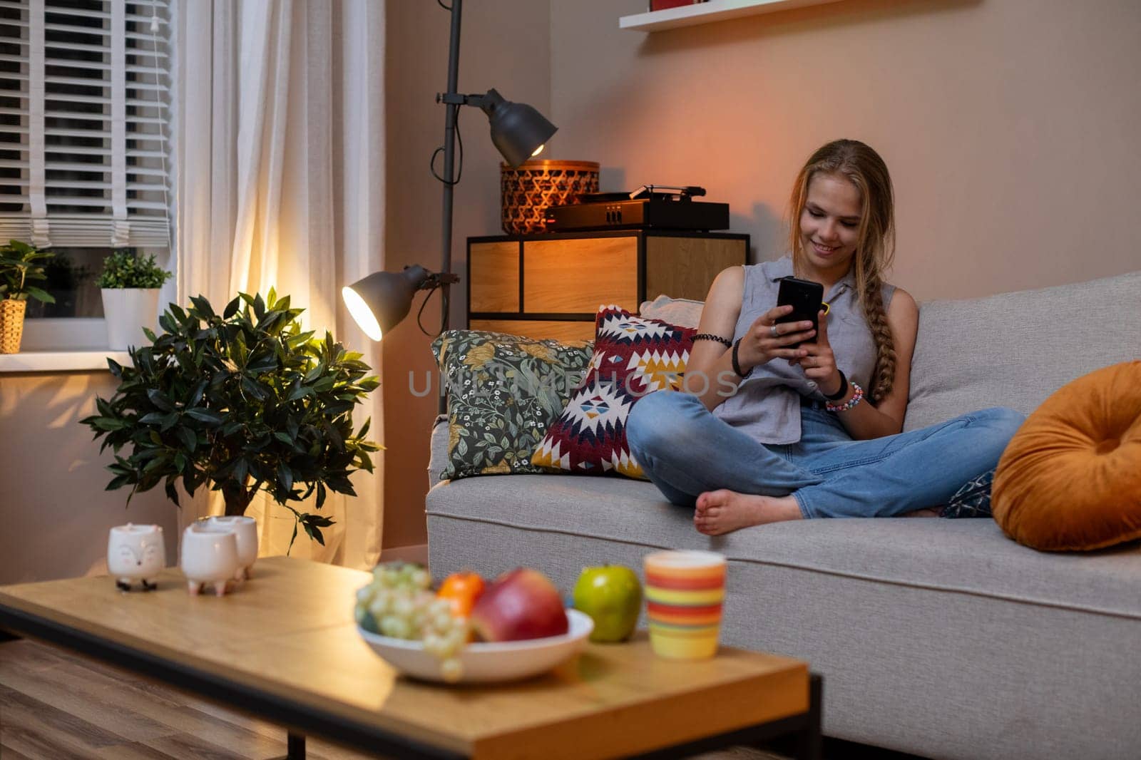 A serene indoor scene of a young woman relaxing on a couch, enjoying snacks and using her smartphone.