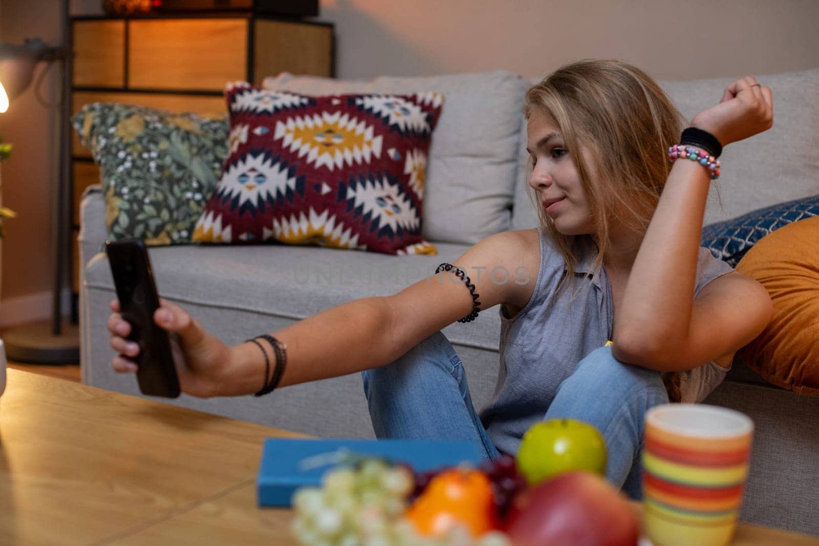 A young woman sits at home, enjoying the moment and capturing it on her phone, with tasty snacks nearby