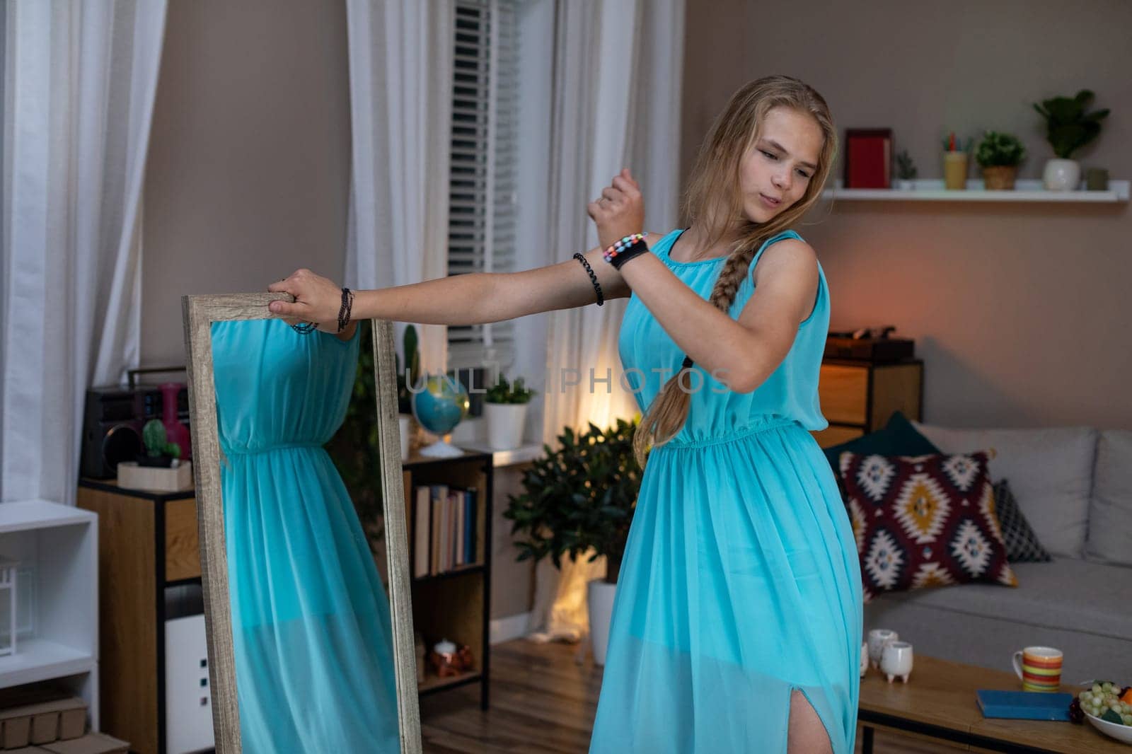A girl in a beautiful blue dress admires her reflection in a cozy, charming room full of style and elegance
