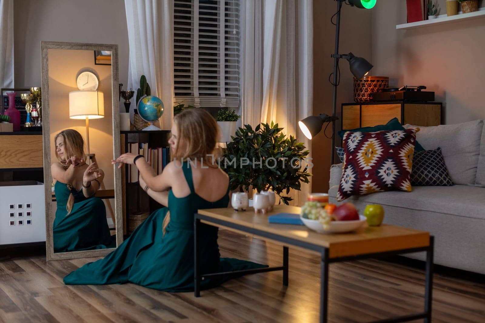 A peaceful evening scene features a woman in a flowing green dress, admiring herself in the elegant mirror
