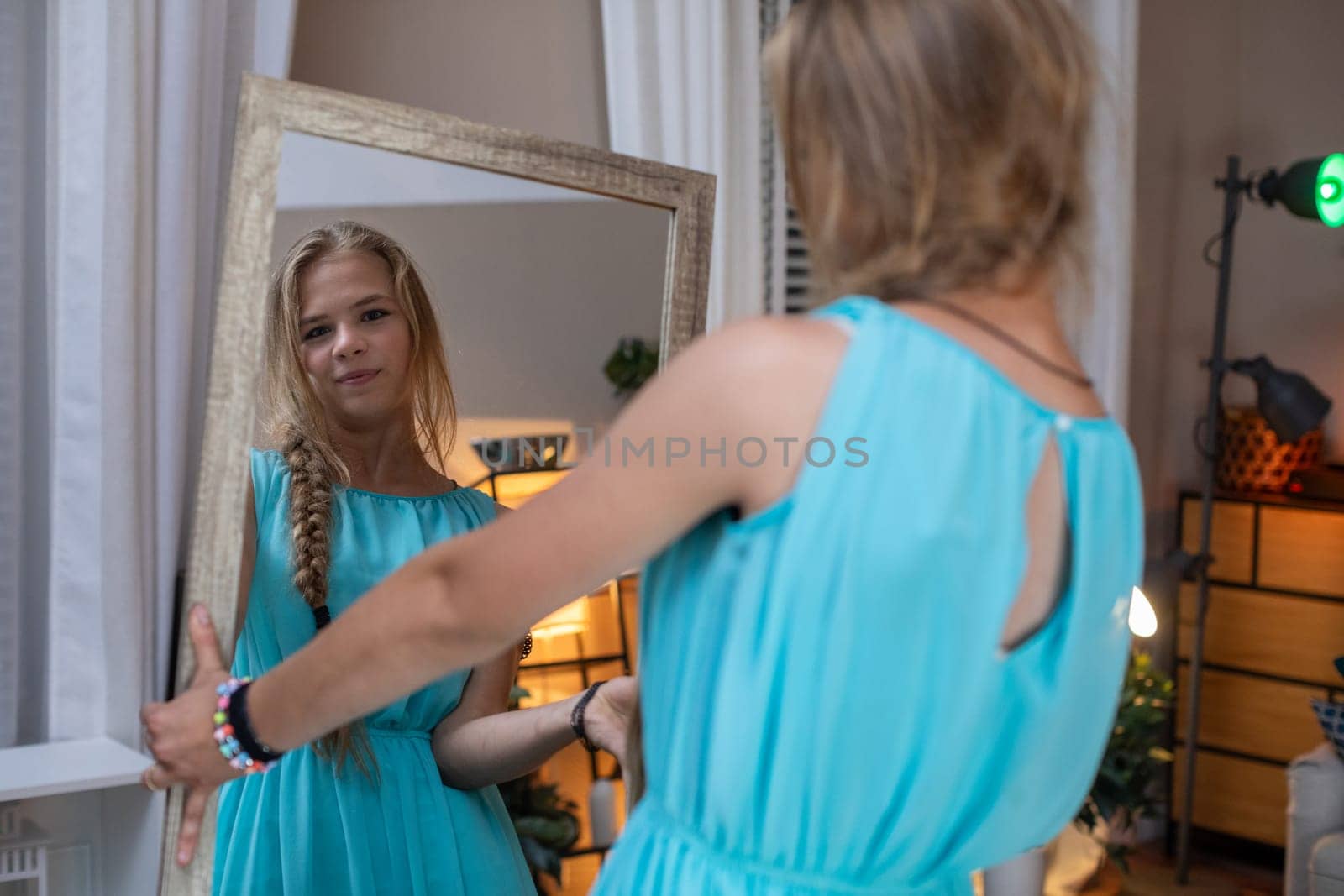 A girl in a turquoise dress gazes thoughtfully into a mirror, capturing a serene and peaceful moment