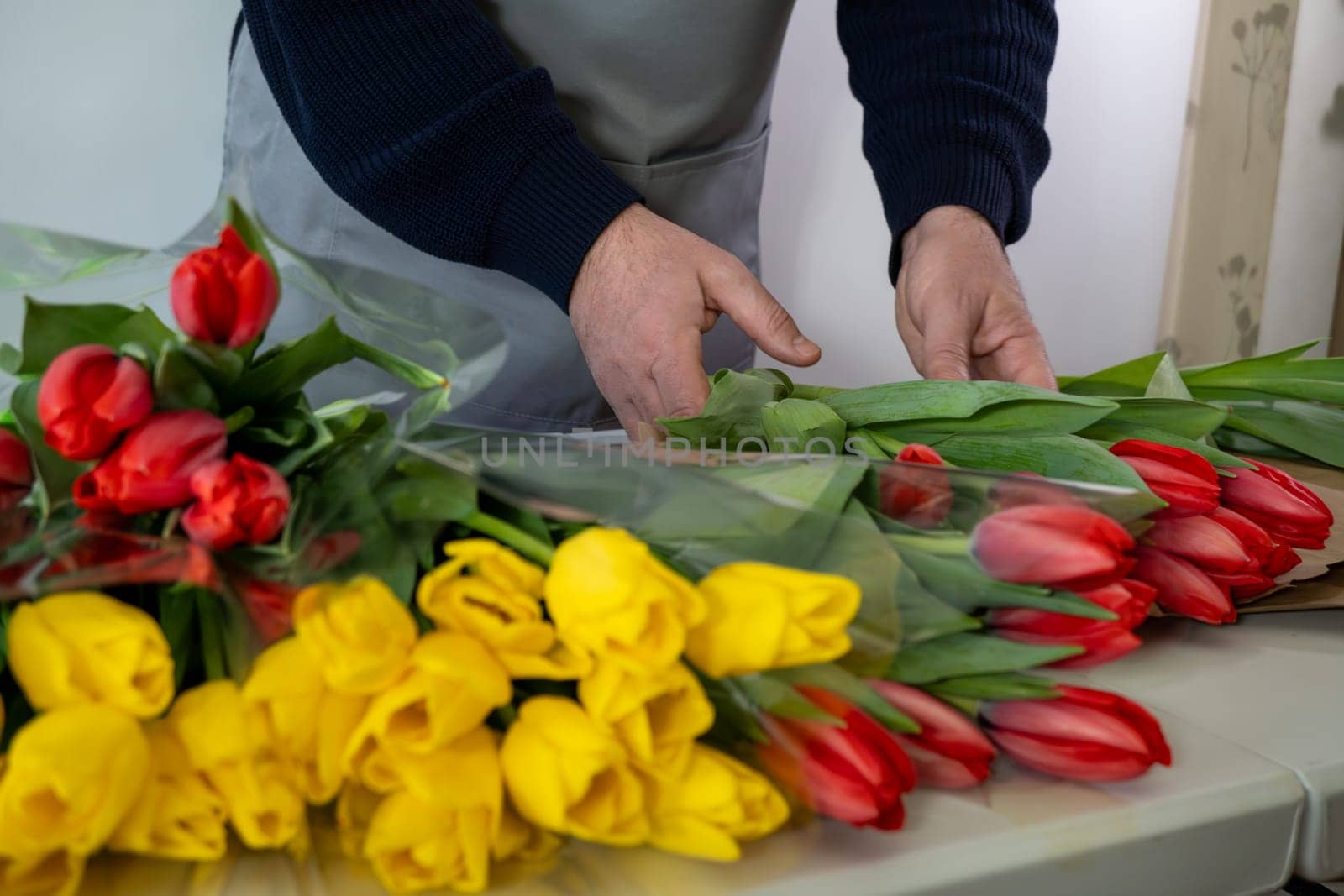 Adult caucasian male arranging red and yellow tulip bouquets on counter.