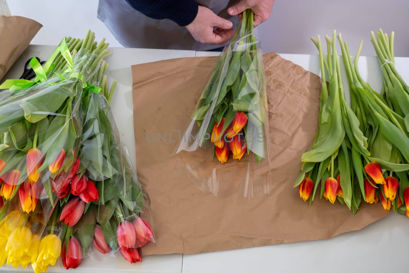 Florist arranging colorful tulip bouquets on wrapping paper.Top view