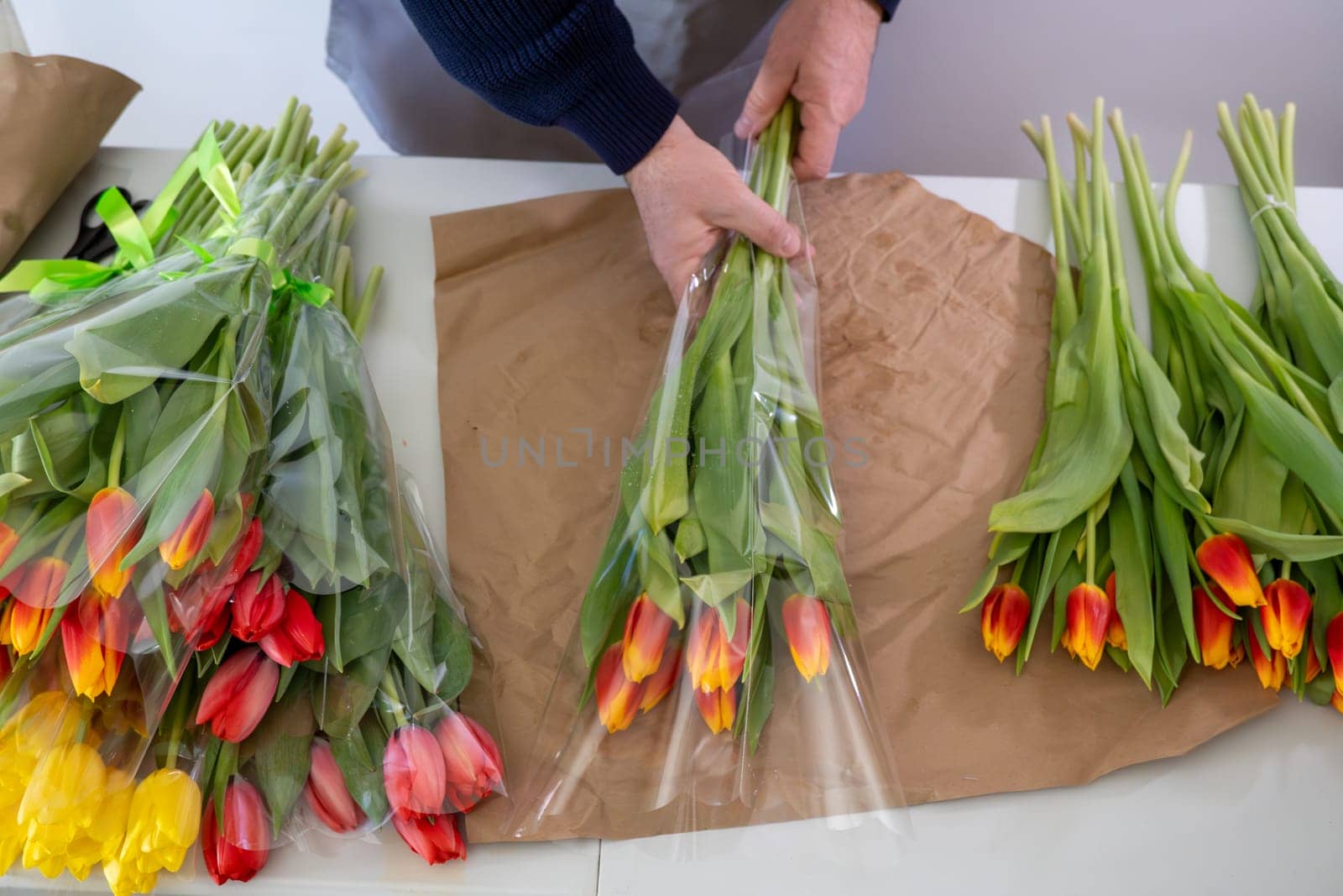 Caucasian male arranging tulips on craft paper: florist working with colorful flowers.Top view