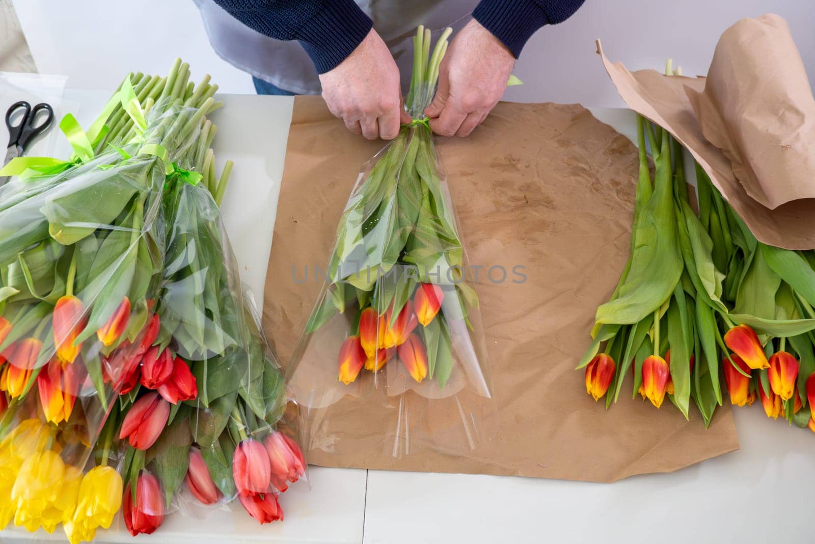 Caucasian male adult arranging vibrant tulip bouquets on craft paper.Top view