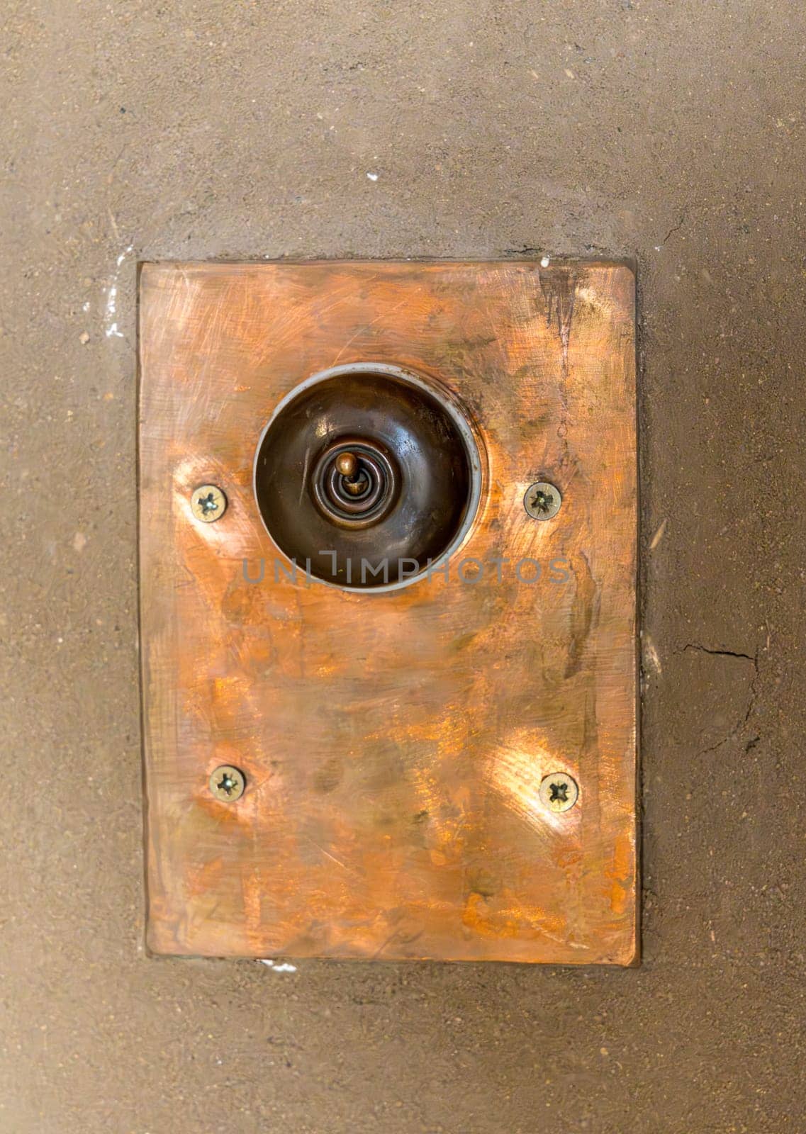 Close up of antique toggle light switch with copper faceplate on textured concrete wall providing vintage, rustic design detail.