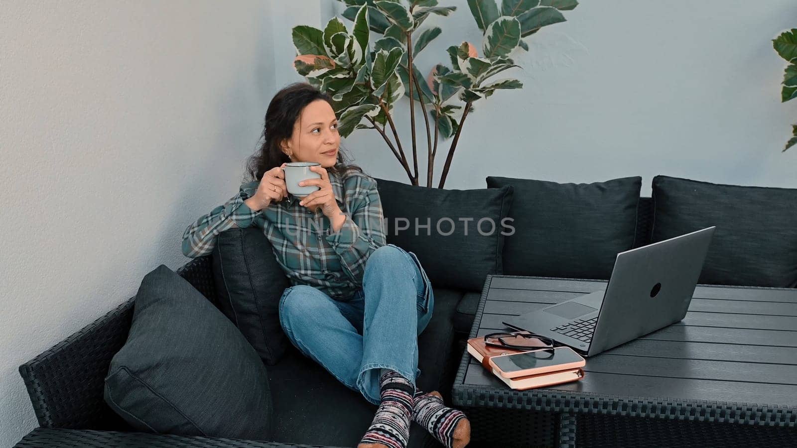 A serene image of a woman enjoying coffee in a cozy setup, illustrating remote work lifestyle. A laptop and personal items nearby emphasize modern work flexibility and leisure.