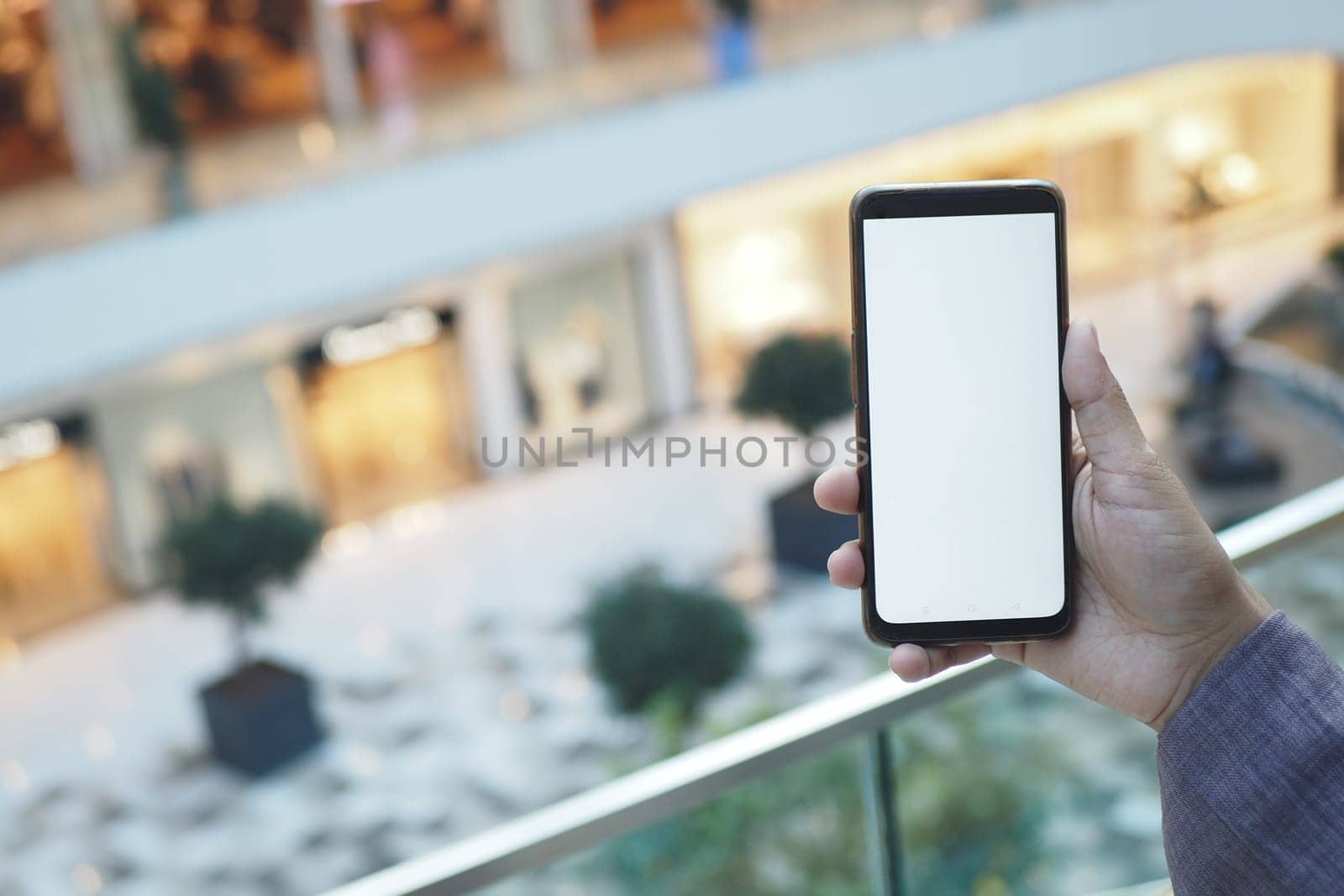 A person displays a blank smartphone screen in a lively mall.