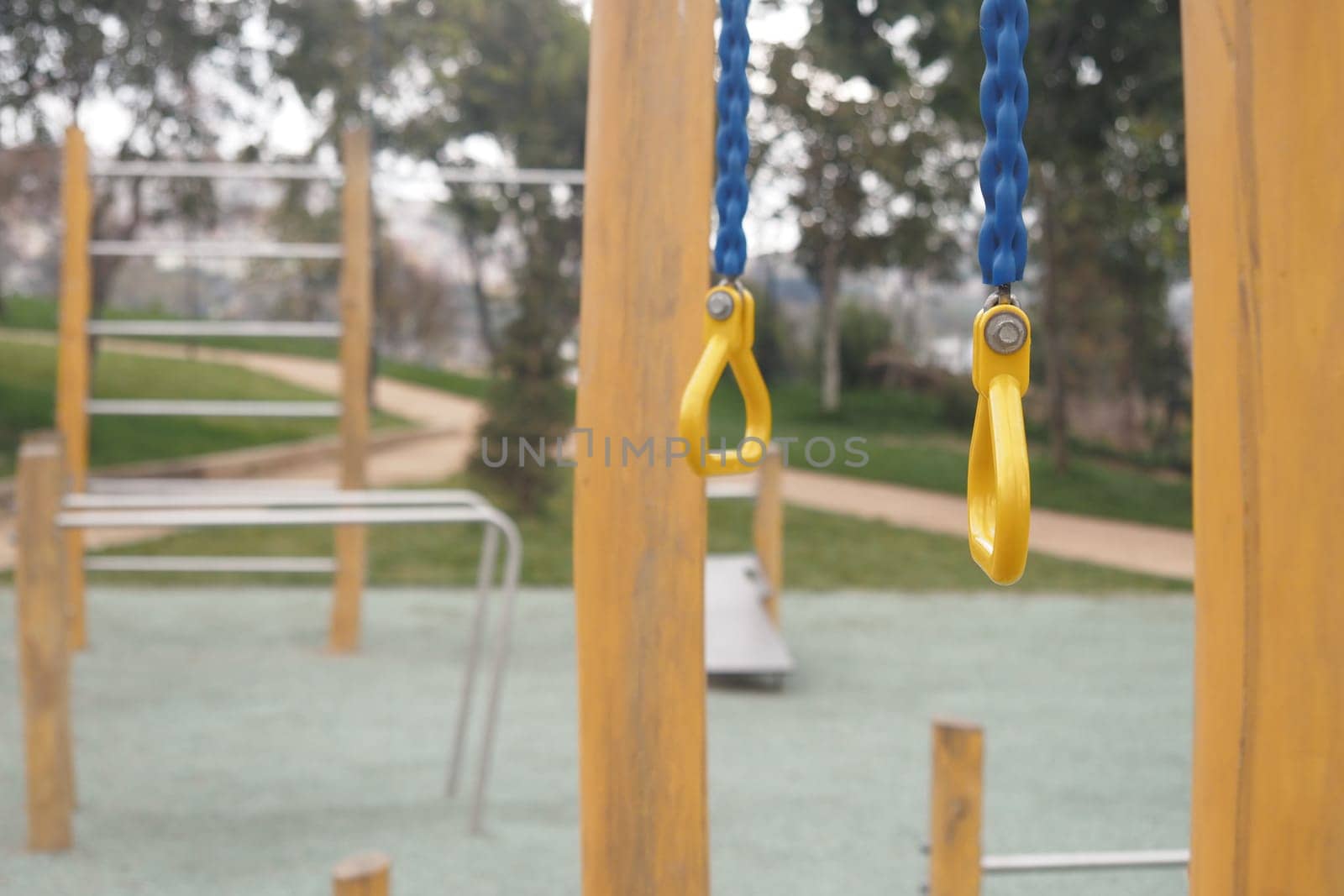 Quiet playground with yellow swings and climbing frames under trees.