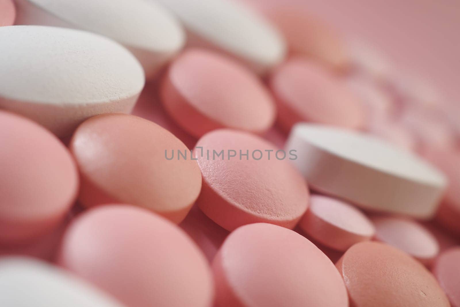 A variety of round tablets in pink and white hues scattered on a surface.