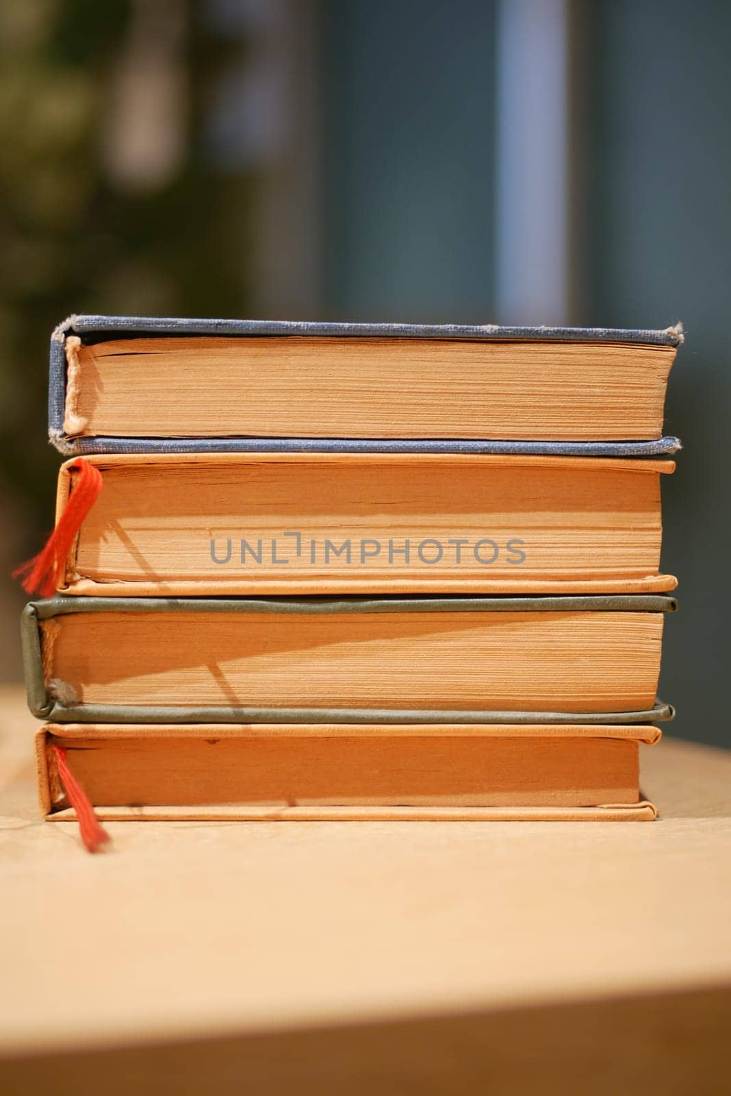 Four vintage books are neatly stacked on a wooden table's surface.