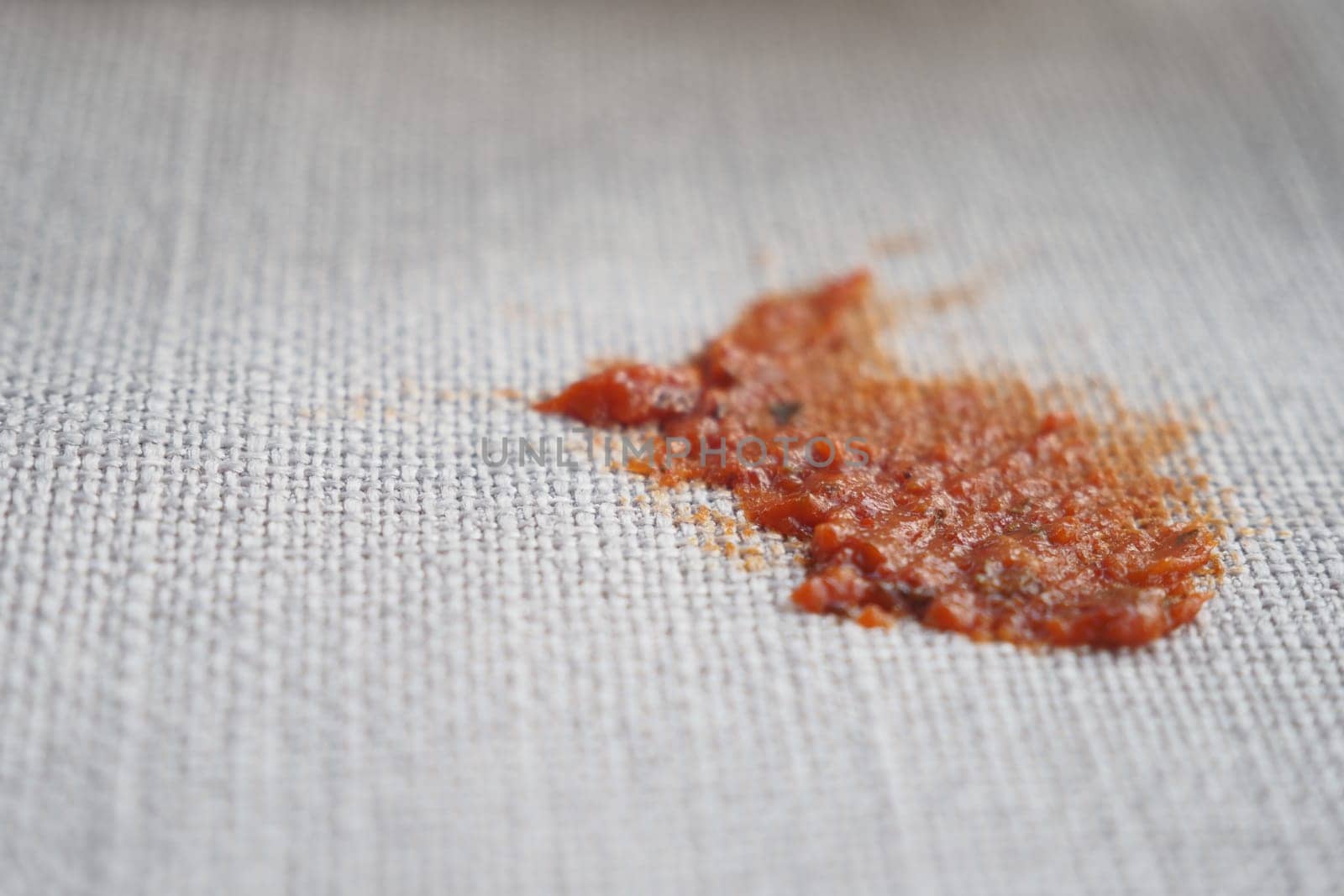A small stain left by spilled tomato sauce on beige fabric.