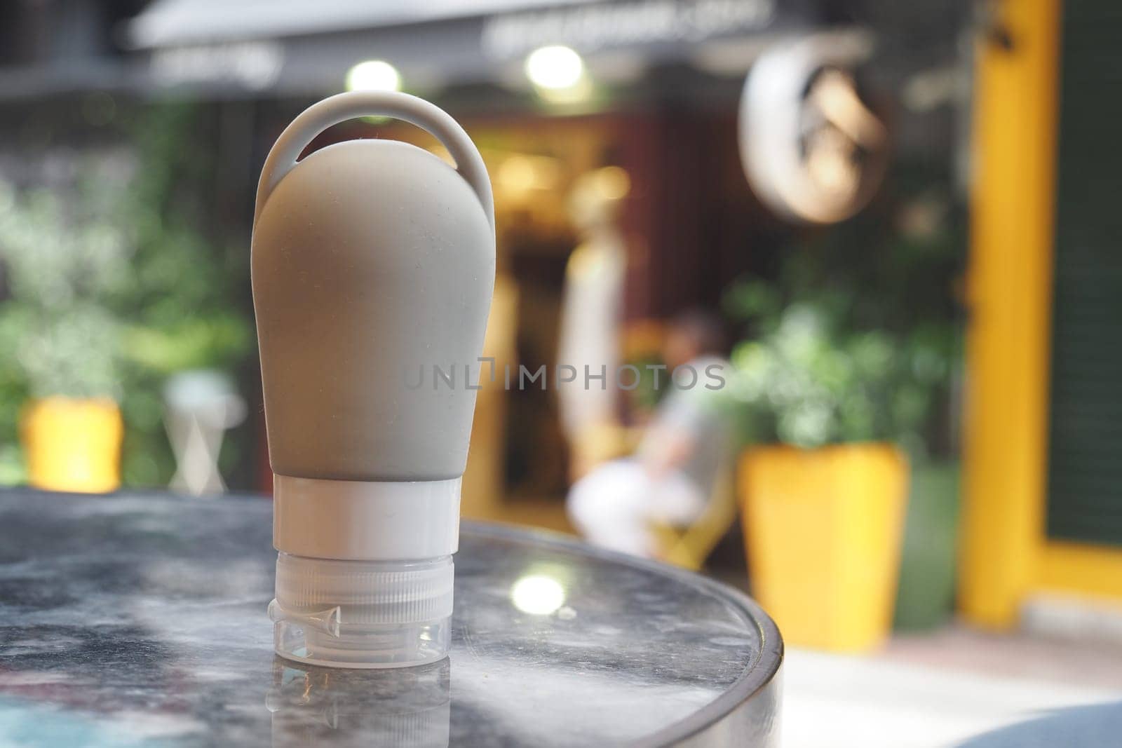 A reusable squeeze bottle sits on a table while people relax nearby.
