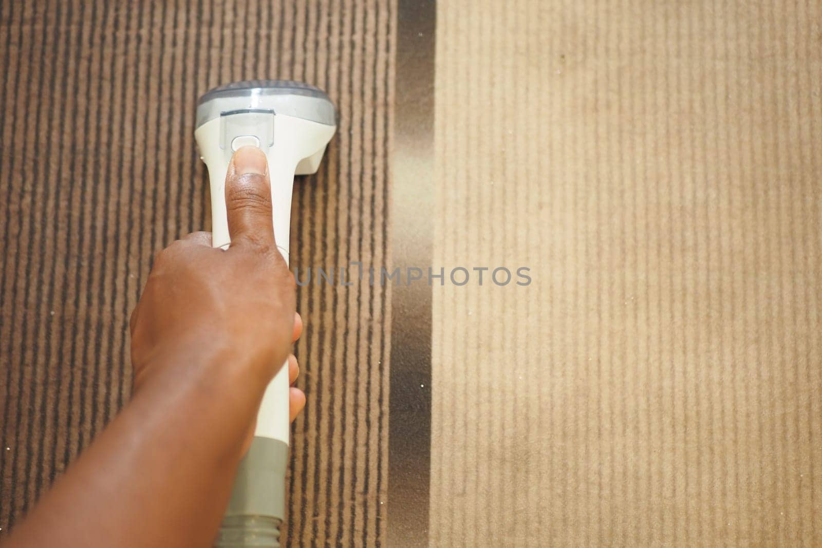 Person uses a handheld cleaner on carpet, focusing on dirt removal.
