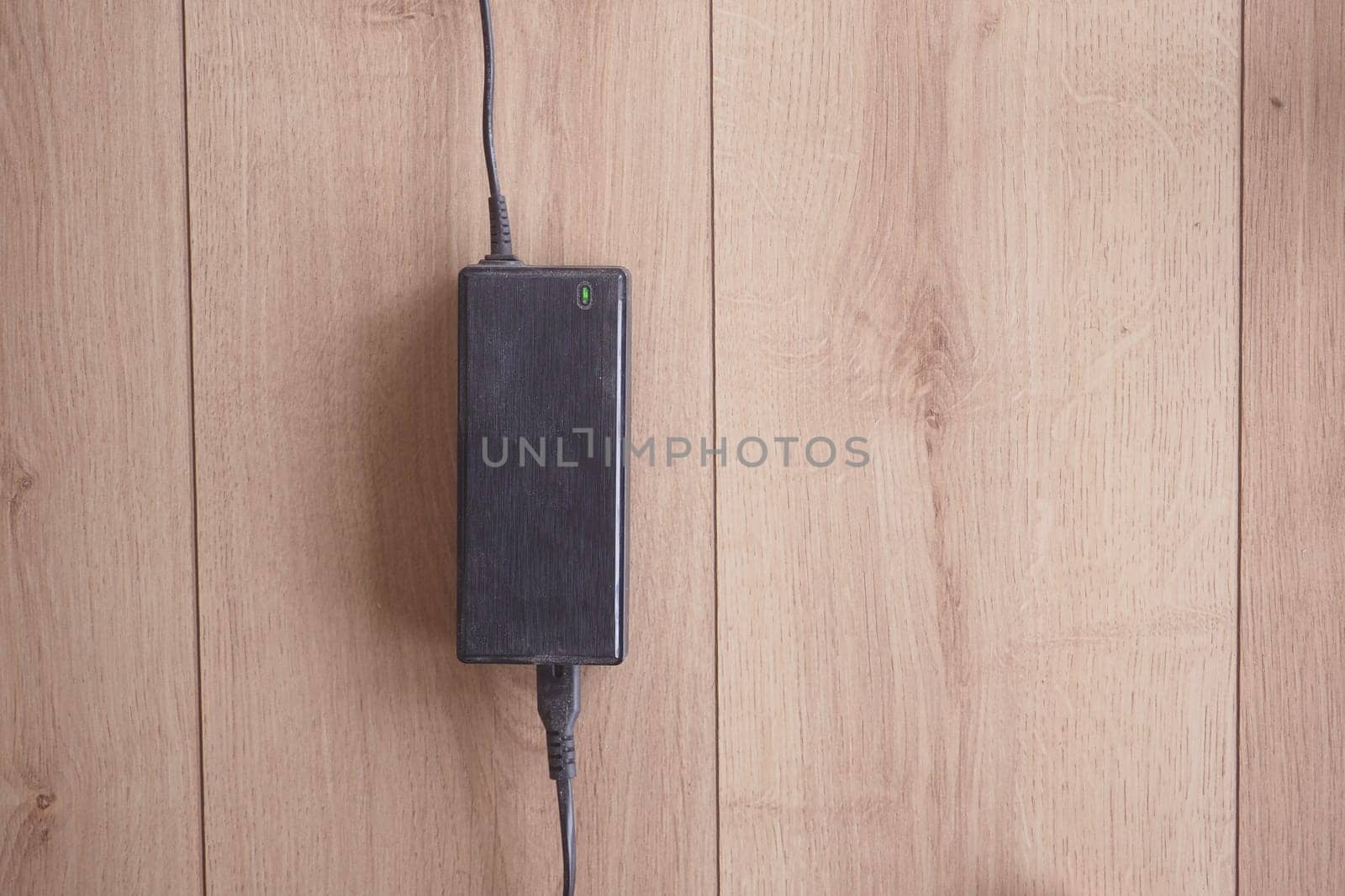 Black power adapter positioned on a light wood background.