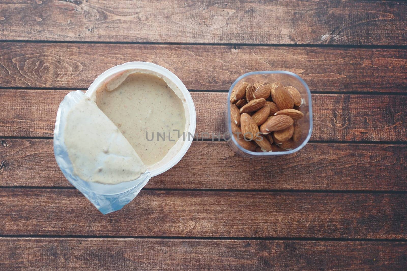 A container of almond butter and a bowl of almonds shown on a table.