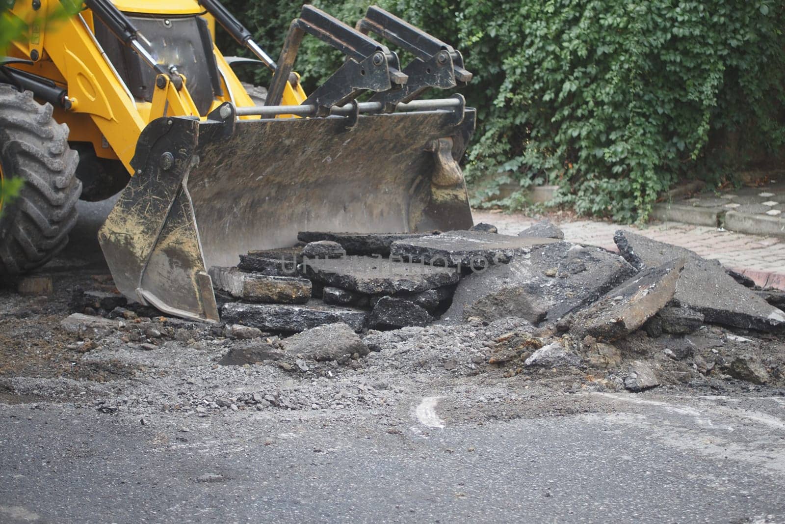 Construction crew uses a loader to lift broken asphalt for repairs.