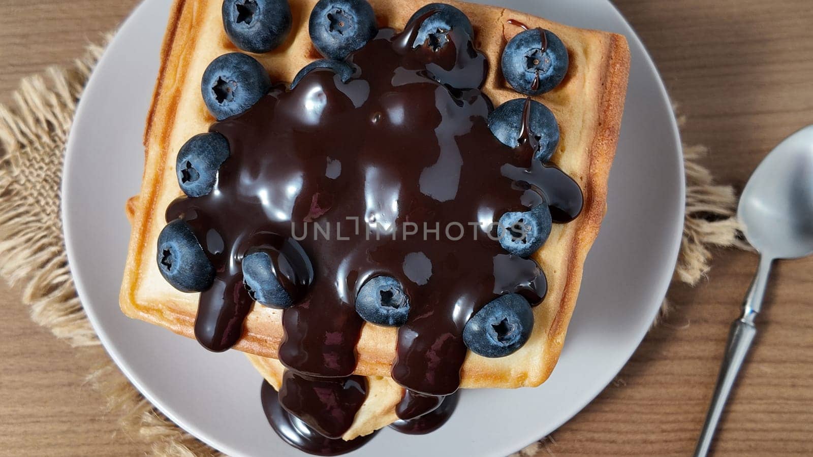 Delicious waffle topped with fresh blueberries and rich chocolate sauce served on a plate.