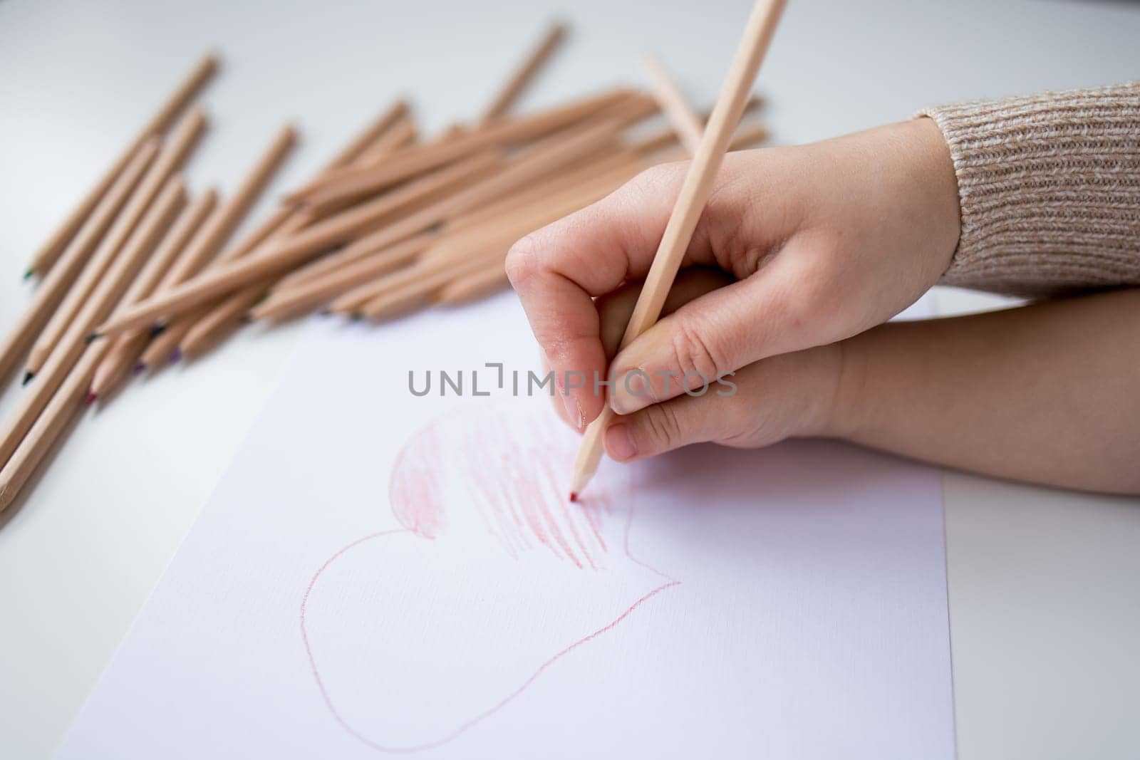Female hand drawing heart with colored pencils on white paper.