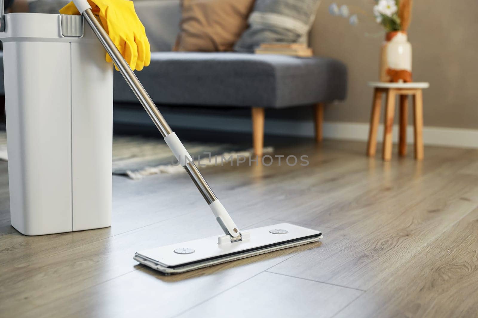 Cleaning supplies: mop, gloves, bucket with wringer sitting on wooden laminate floor in modern living room, wet equipment tools, housekeeping concept. Emphasizing home sanitation, cleanliness, hygiene