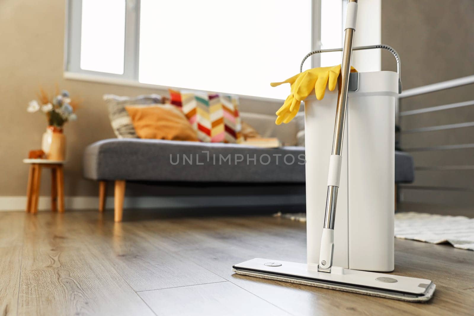 Cleaning supplies: mop, gloves, bucket with wringer sitting on wooden laminate floor in modern living room, wet equipment tools, housekeeping concept. Emphasizing home sanitation, cleanliness, hygiene