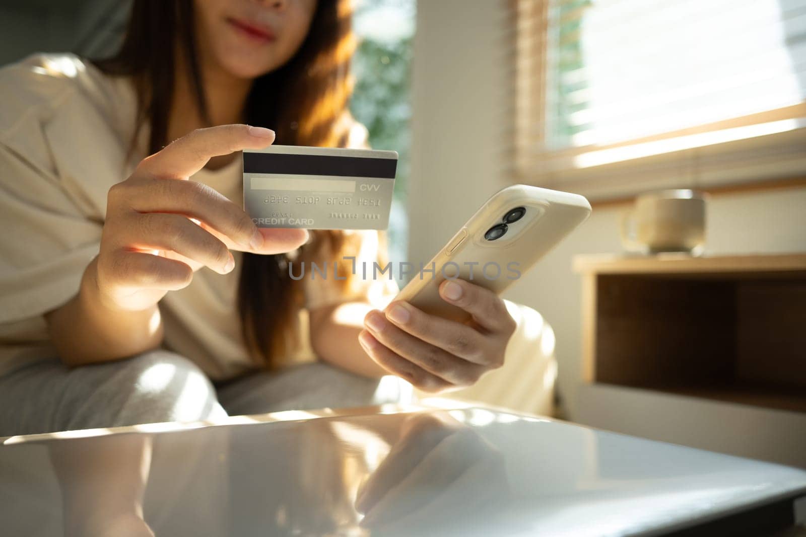 Woman holding credit card while using smartphone for online transactions or digital payments.